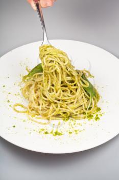eating spaghetti mixed with fresh pesto from white plate