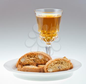 crystal glass with sweet white wine and italian almond cantuccini on saucer on grey background