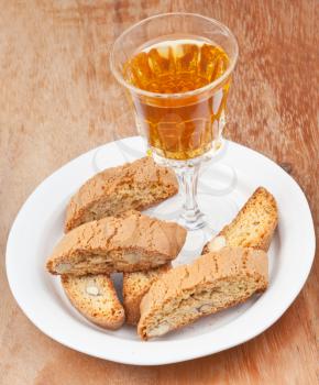 wineglass with sweet white wine and italian almond cantuccini on saucer on wooden table