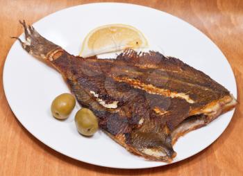 fried sole fish on white plate on wooden table