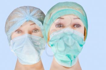 two women's dummy doctor heads wearing textile surgical cap and medical protective mask isolated on blue background