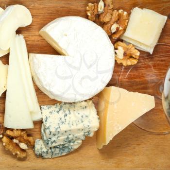 glass and assortment of cheeses on wooden plate close up