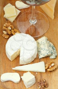 red wine glass and sliced cheeses on wooden plate close up