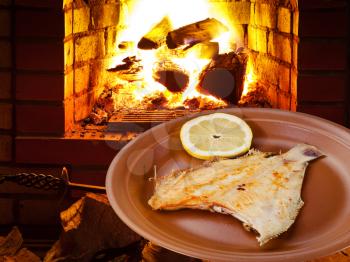 fried sole fish on plate and open fire in wood burning oven