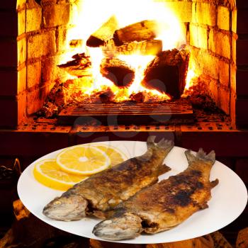 fried river trout fish on plate and open fire in wood burning oven