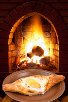 adzharian khachapuri with egg on plate and open fire in wood burning stove