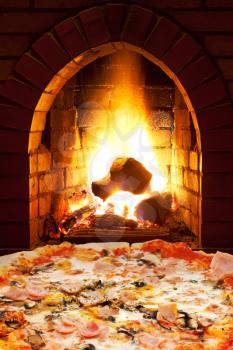 italian pizza with ham and mushrooms and open fire in wood burning stove