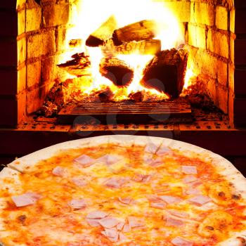 italian pizza with prosciutto cotto and open fire in wood burning stove