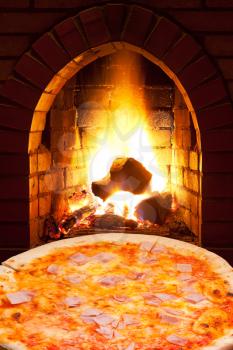 italian pizza with ham and open fire in wood burning oven
