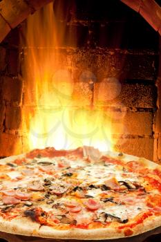 italian pizza with ham and mushrooms and fire flames in wood burning oven