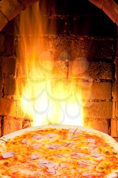italian pizza with prosciutto cotto and fire flames in wood burning oven