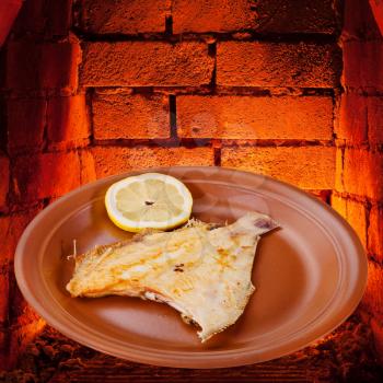fried sole fish on plate and hot bricks of wood burning oven