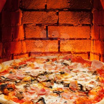 italian pizza with ham and mushrooms and hot brick wall of wood burning oven