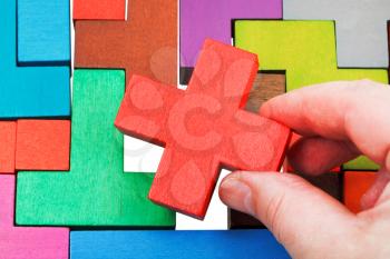putting cross shaped piece in wooden multicoloured puzzle isolated on white background