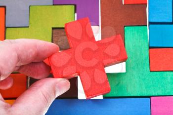 putting cross shaped block in wooden multicoloured puzzle isolated on white background