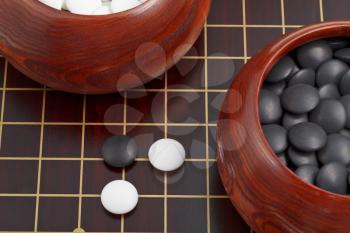 black and white go game stones and wooden bowls on goban