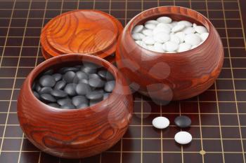 black and white go game stones and wooden bowls on wood board