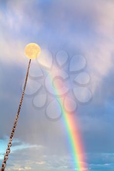 yellow full moon tied on chain soars into sky with rainbow