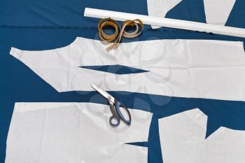 tailor tools and paper sample of clothes on blue fabric for dress cutting