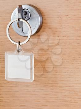 one steel key with blank square keychain in lock of wooden door close up