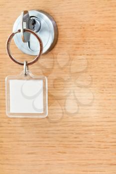 home key with blank square keychain in lock of wooden door close up