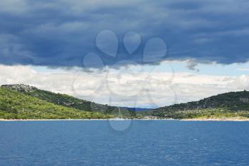 green coastline of Adriatic Sea in Dalmatia under dark blue clouds, Croatia