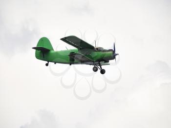 small green airplane flying in overcast sky in summer day