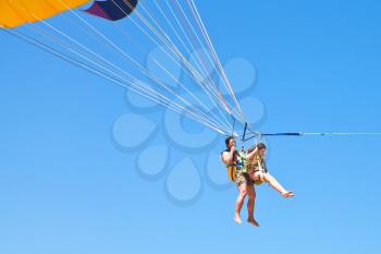 man and girl parasailing on parachute in blue sky in summer day