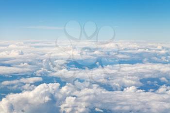 horizon above white clouds in blue sky and lands under clouds