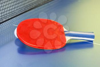 red bat, tennis ball on blue ping pong table close up