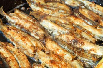 fried fish capelin on black frying pan close up