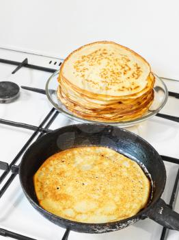 fried pancake in pan and stack of prepared pancakes