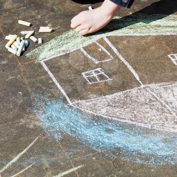 girl paints a house with colored chalk on asphalt outdoors