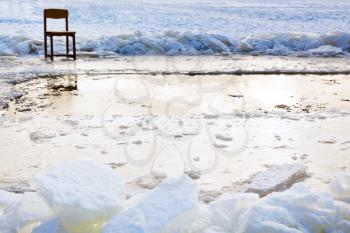 icebound chair near ice hole in frozen lake in cold winter day