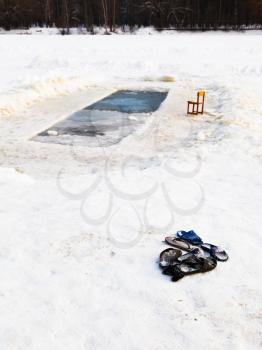 slippers and chair near ice hole in frozen lake in cold winter day
