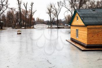 frozen pond with footbridge and wooden house on winter day