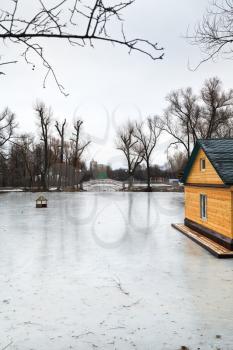 frozen pond with footbridge in urban park in winter day