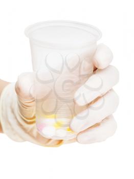 gloved hand holding plastic cup with tablets isolated on white background