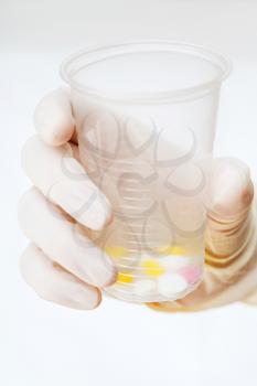 gloved hand holding plastic cup with tablets on white background