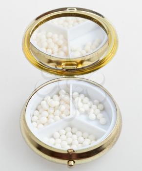 compact pill box with sugar homeopathy balls on white background
