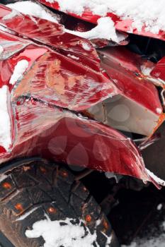 broken fender and crumpled hood of red car after winter traffic accident