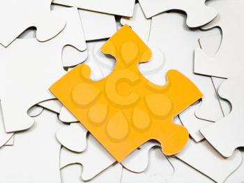one yellow piece of puzzle on pile of white jigsaw puzzles