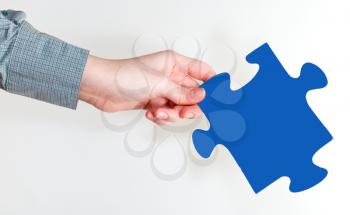 female hand holding blue puzzle piece on grey background
