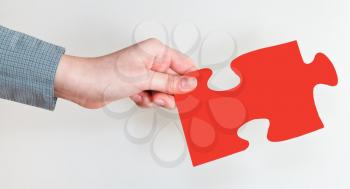 female hand holding red puzzle piece on grey background