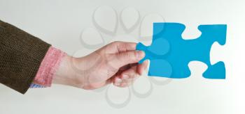 blue puzzle piece in male hand on grey background