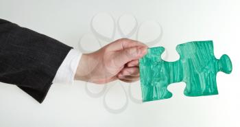 green painted puzzle piece in male hand on grey background