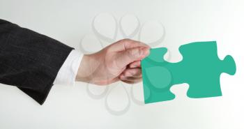 male hand holding green puzzle piece on grey background