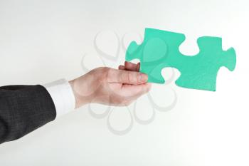 green puzzle piece in male hand on grey background