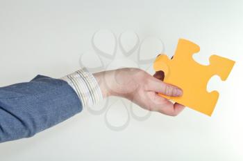 yellow puzzle piece in male hand on grey background