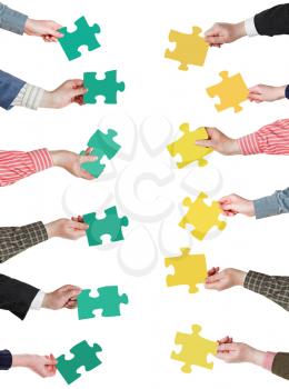 set of green and yellow puzzle pieces in opposite sides in people hands isolated on white background